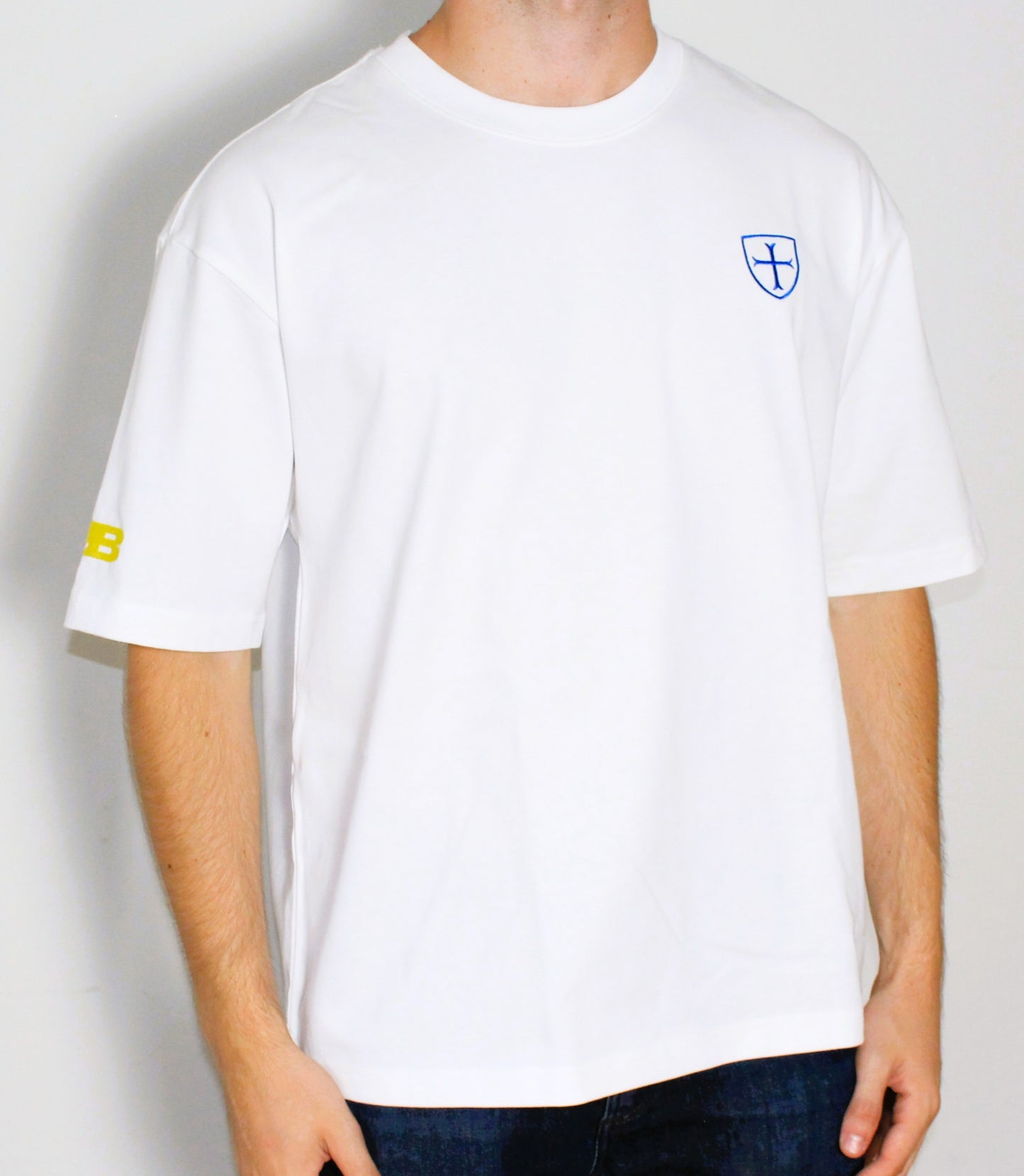 White t-shirt with a logo on the chest and sleeve, worn by a person against a plain background