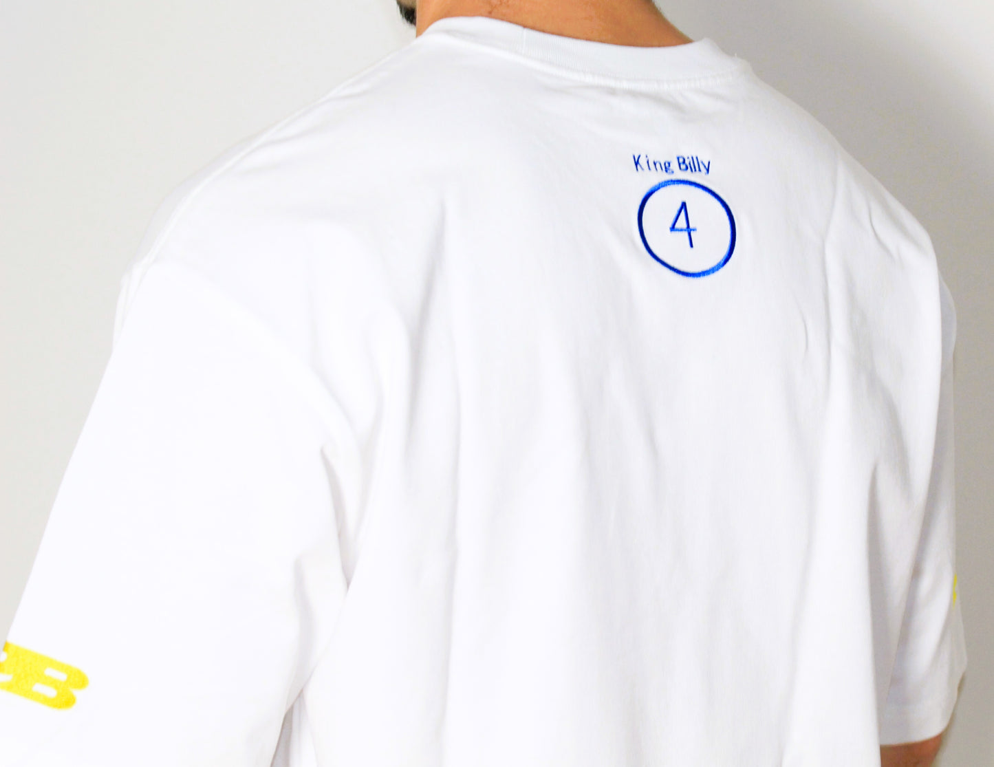 White t-shirt with blue logo and text on the back, worn by a person.