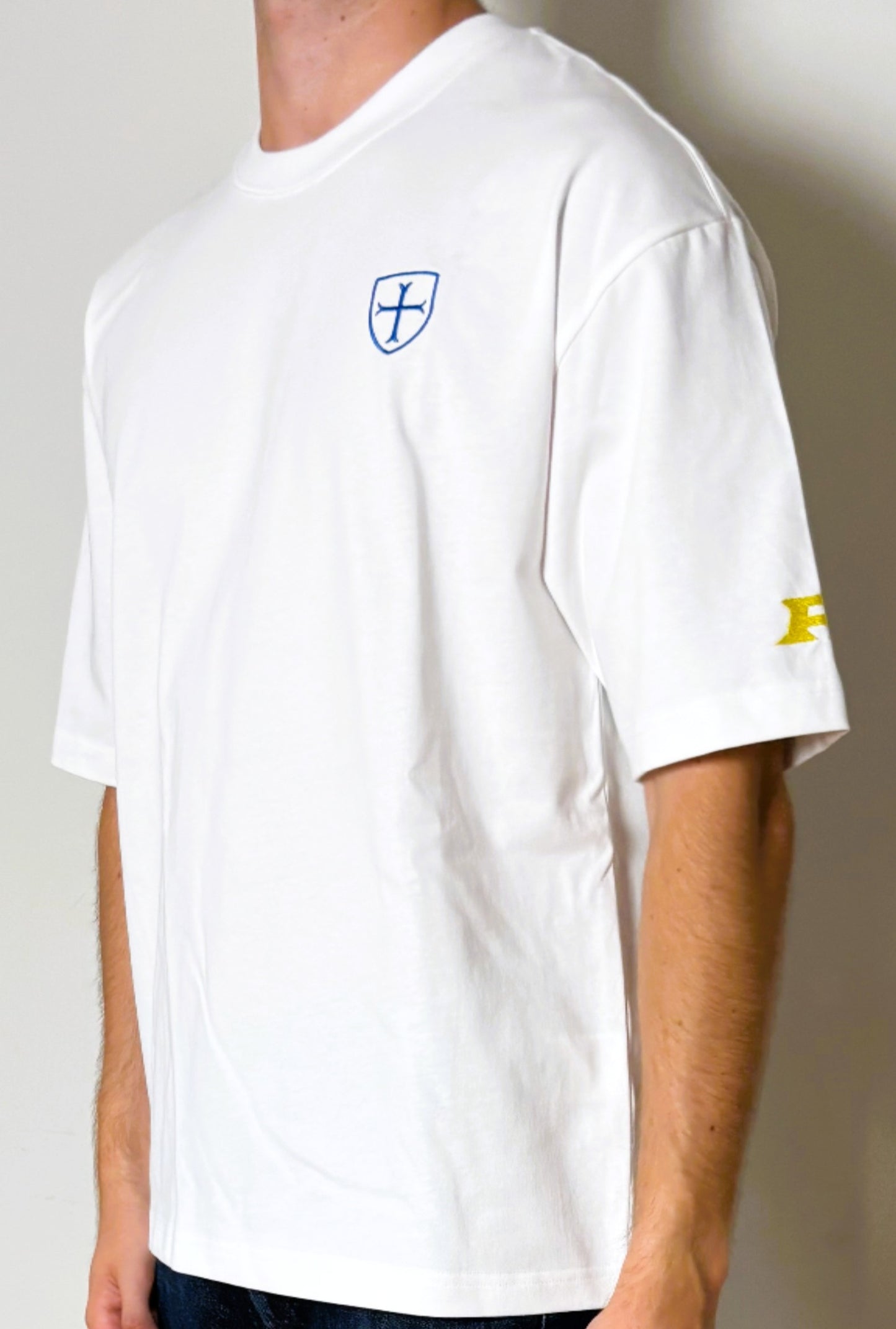 White t-shirt with a logo on the chest and another on the sleeve against a neutral background