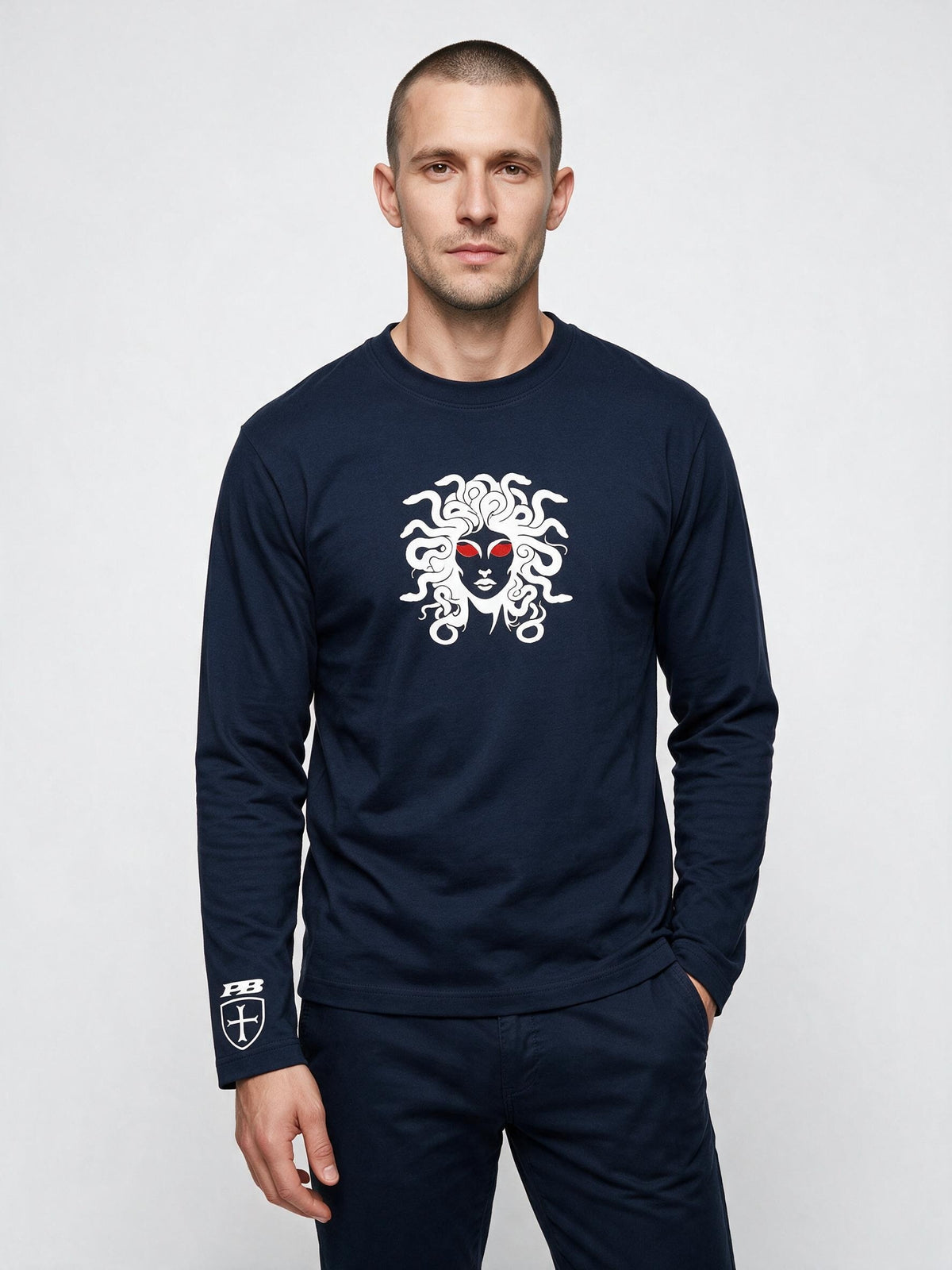 A man wearing a navy blue long-sleeve crewneck shirt with a large white Medusa graphic on the chest and a Versace logo on the left sleeve, paired with matching navy pants, against a light gray studio background.