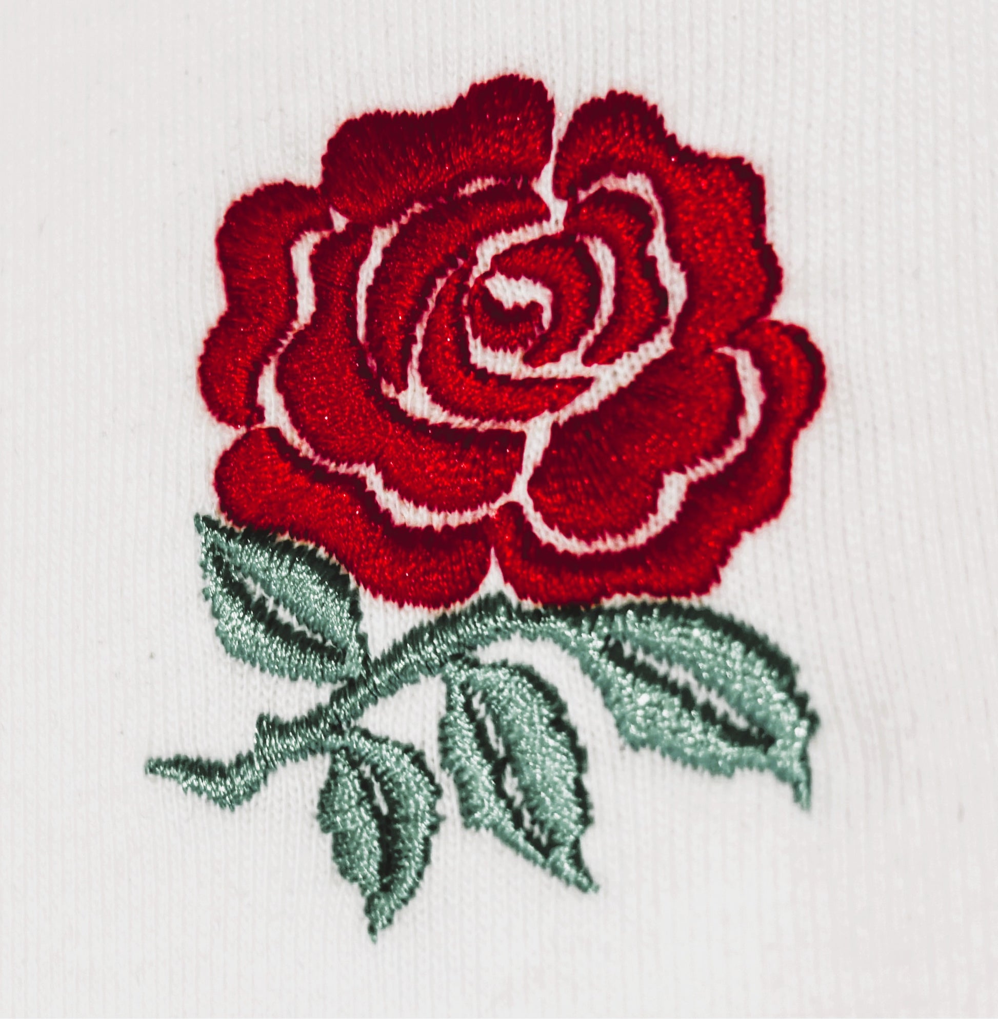 Embroidered red rose with green leaves on a white background