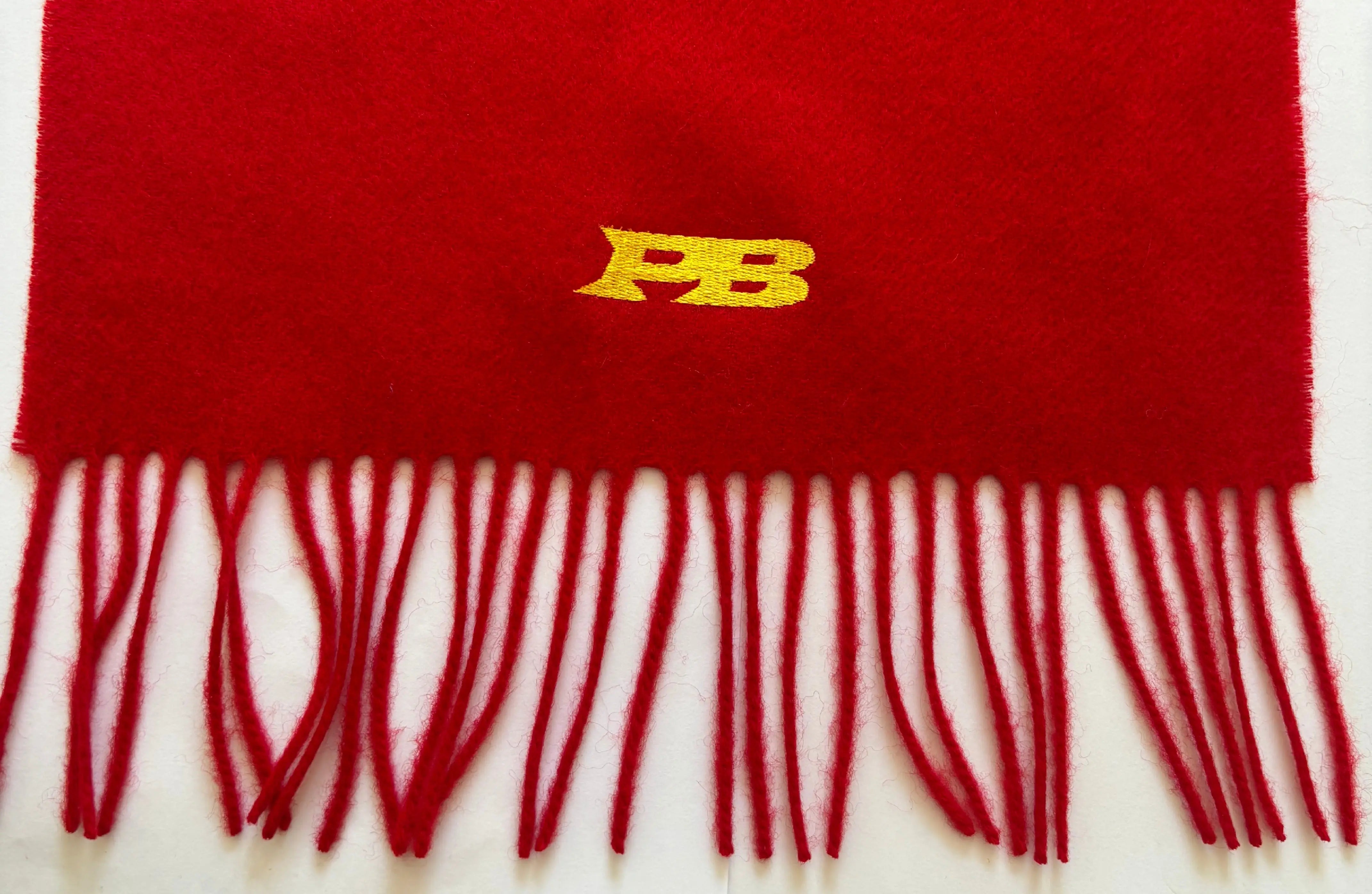 Red merino scarf with white fringe and yellow logo on a white background